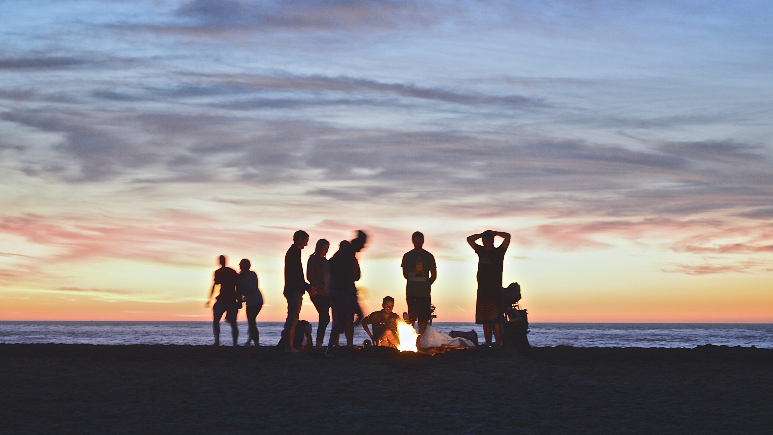 Silhouetten von jungen Menschen am Strand mit Lagerfeuer