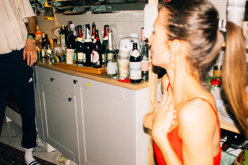 Komfortzone Fragezeichen Eine Küchenzeile voller leerer Alkoholflaschen und Müll, davor unscharf eine tanzende junge Frau