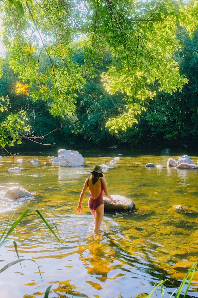 Frau im Badeanzug geht langsam in einen Fluss, die Sonne scheint